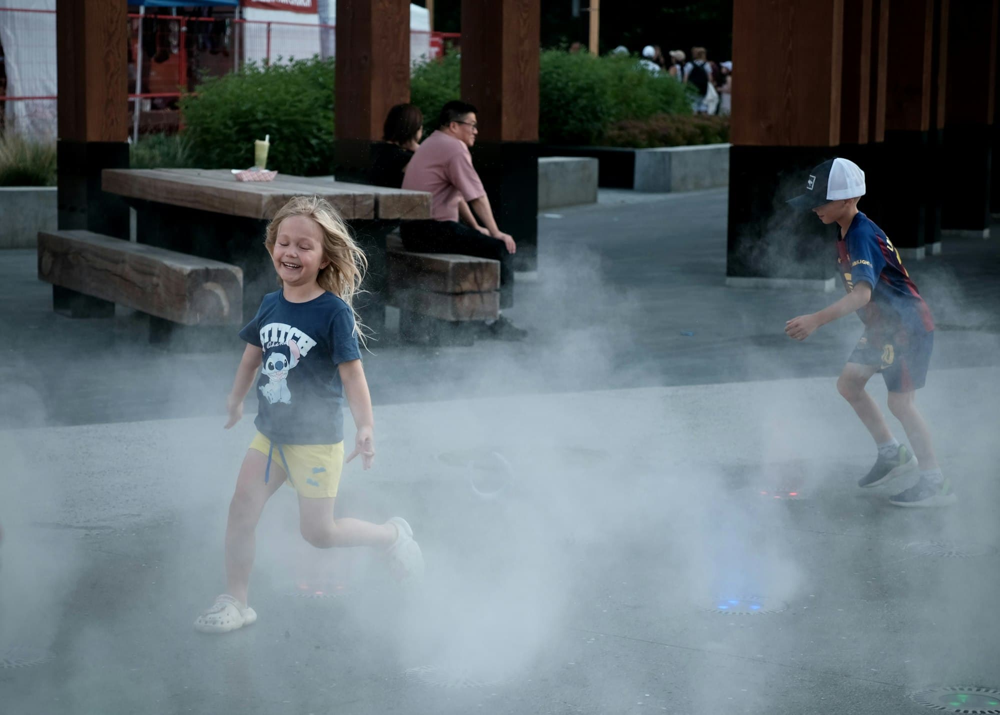 A girl and a boy laughing as they run through cooling mist